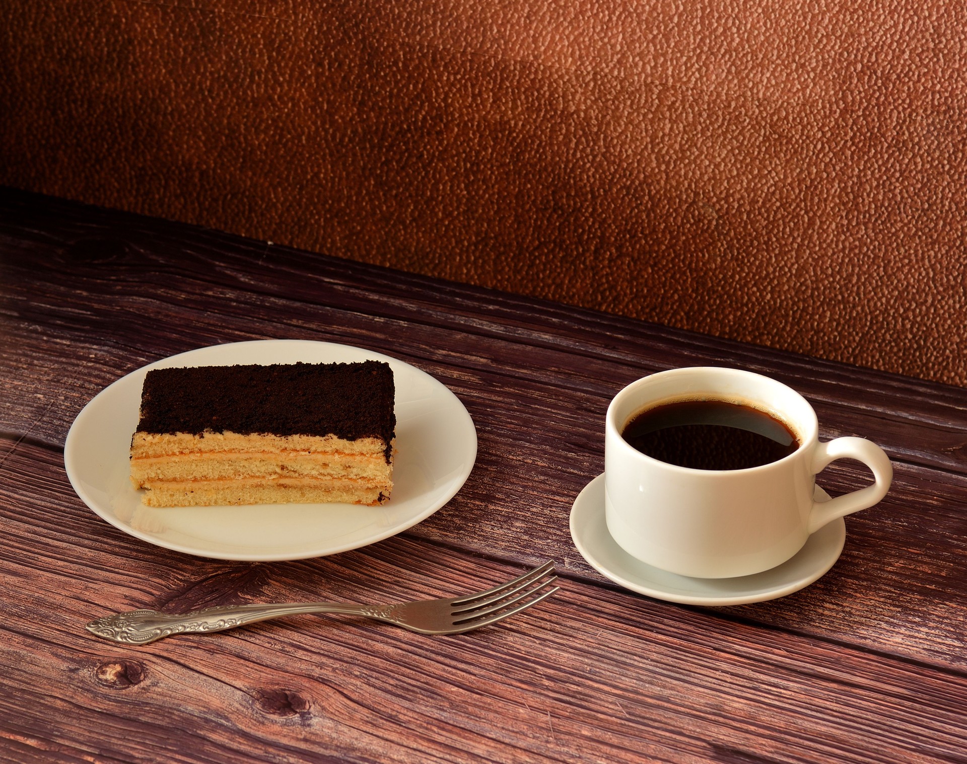 Un pezzo di Tiramisù da dolce italiano, una tazza di caffè nero e una forchetta da tavola su un tavolo di legno.